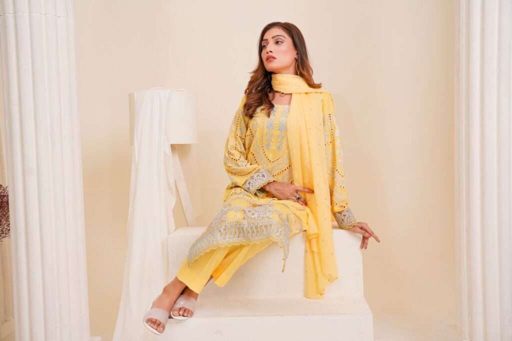 A woman poses elegantly in traditional yellow attire during a studio shoot in Lahore.