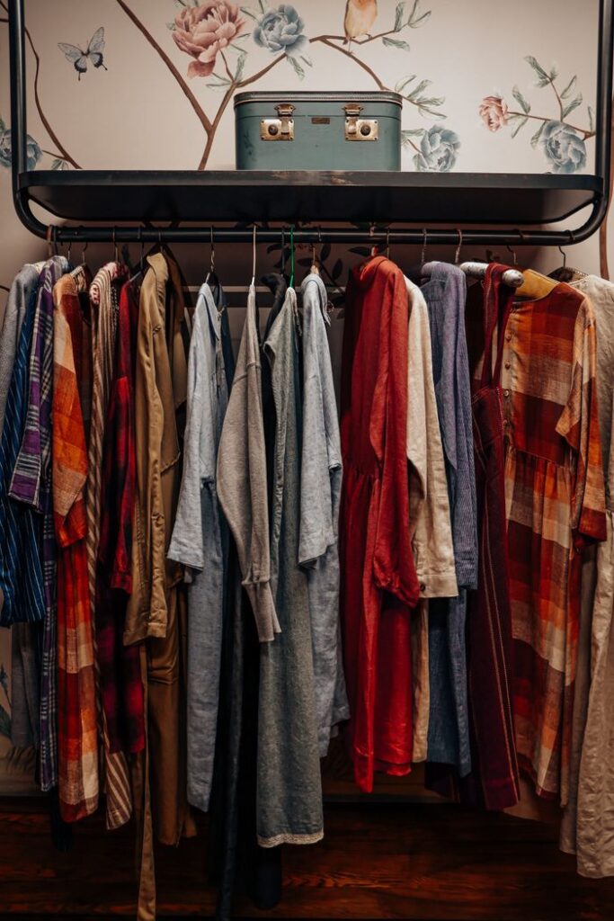 A vibrant selection of vintage clothes neatly hung in a boutique with floral wallpaper backdrop.