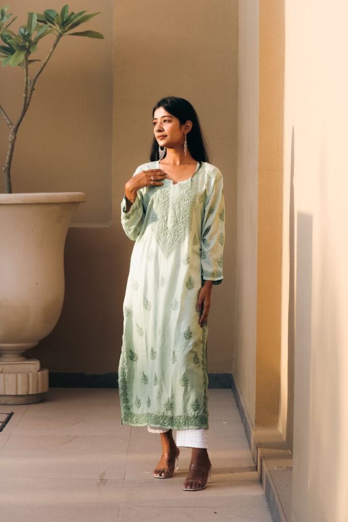 South Asian woman in traditional pistachio green chikankari kurti, enjoying a serene moment indoors.