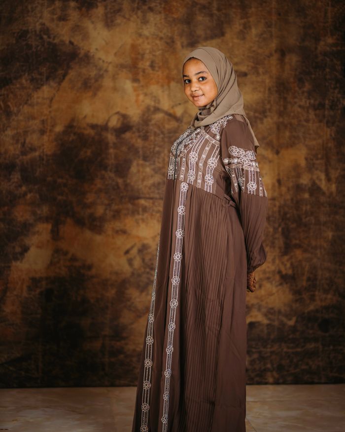 Portrait of a young woman in traditional Islamic clothing with a textured backdrop.