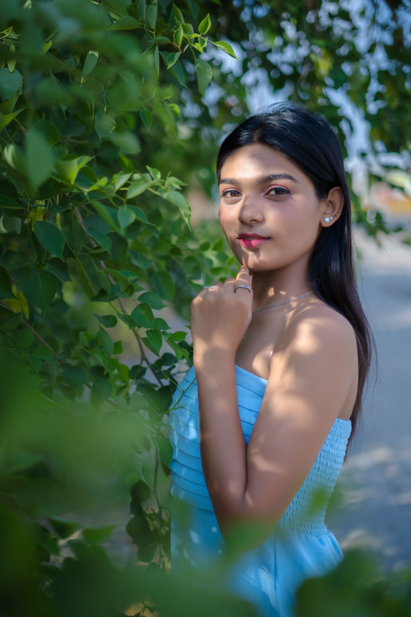 Elegant portrait of a young woman surrounded by lush greenery in a natural setting.